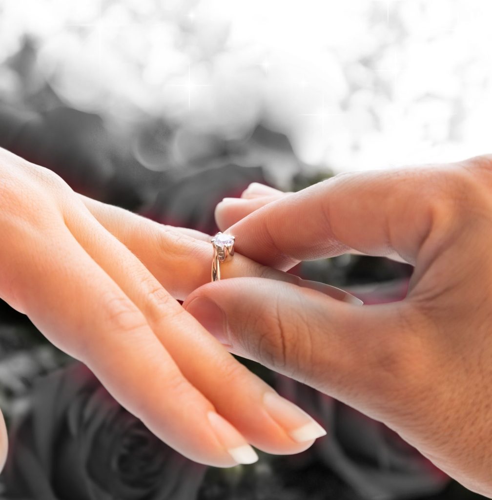 Ein Mann steckt einer Frau einen goldenen Verlobungsring mit Edelstein an den Finger – romantischer Heiratsantrag, Liebe und Verlobung